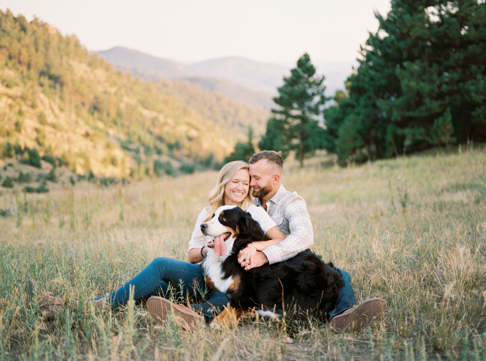 Couple and Bernese mountain dog sitting in field with mountain view at Mount Falcon West