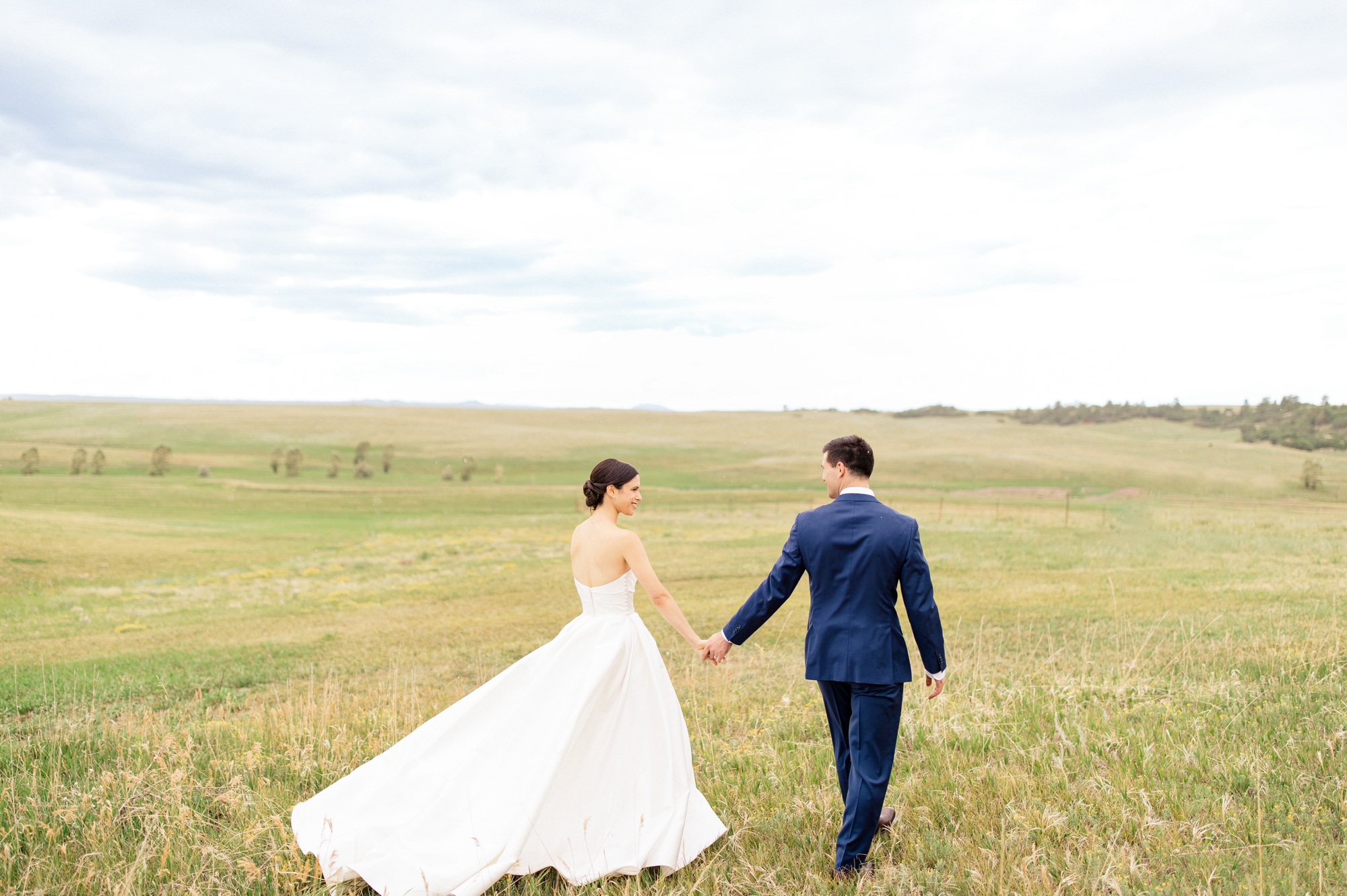 Bride & Groom portrait walking in green field at Flying Horse Ranch Wedding Venue in Colorado Springs