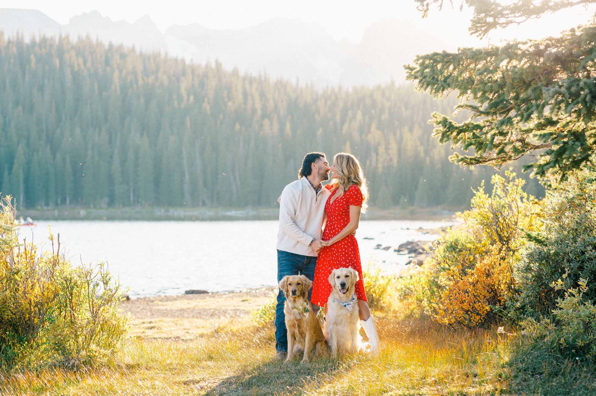 Couple with two golden retriever dogs in engagement photo at Brainard Lake, Colorado mountains and lake backdrop